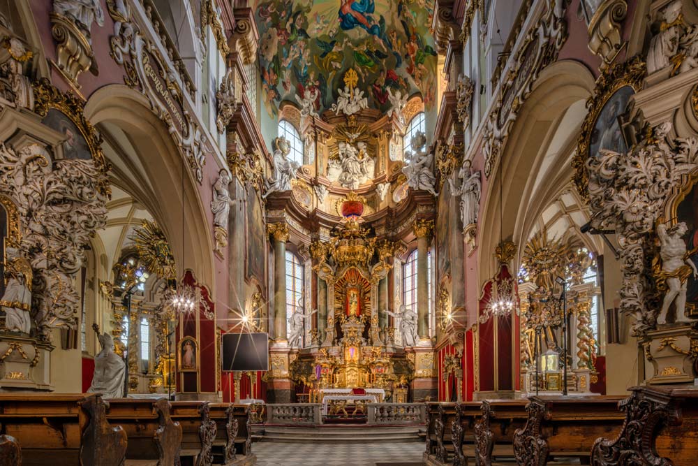 Barokowe wnętrze kościoła Wniebowzięcia NMP w Kłodzku z bogato zdobionym ołtarzem, rzeźbami aniołów i malowidłami na sklepieniu
