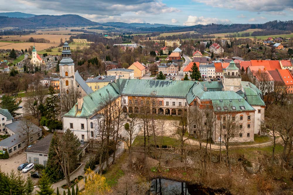 Zamek w Międzylesiu z lotu ptaka — zielone dachy, arkadowe krużganki i panorama miasteczka na tle gór